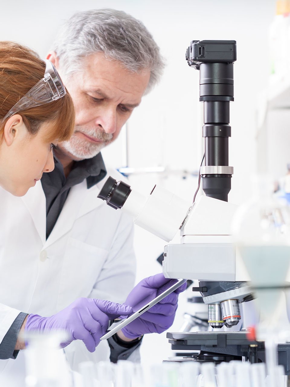 Schülerin und Chemikant stehen an einem Mikroskop