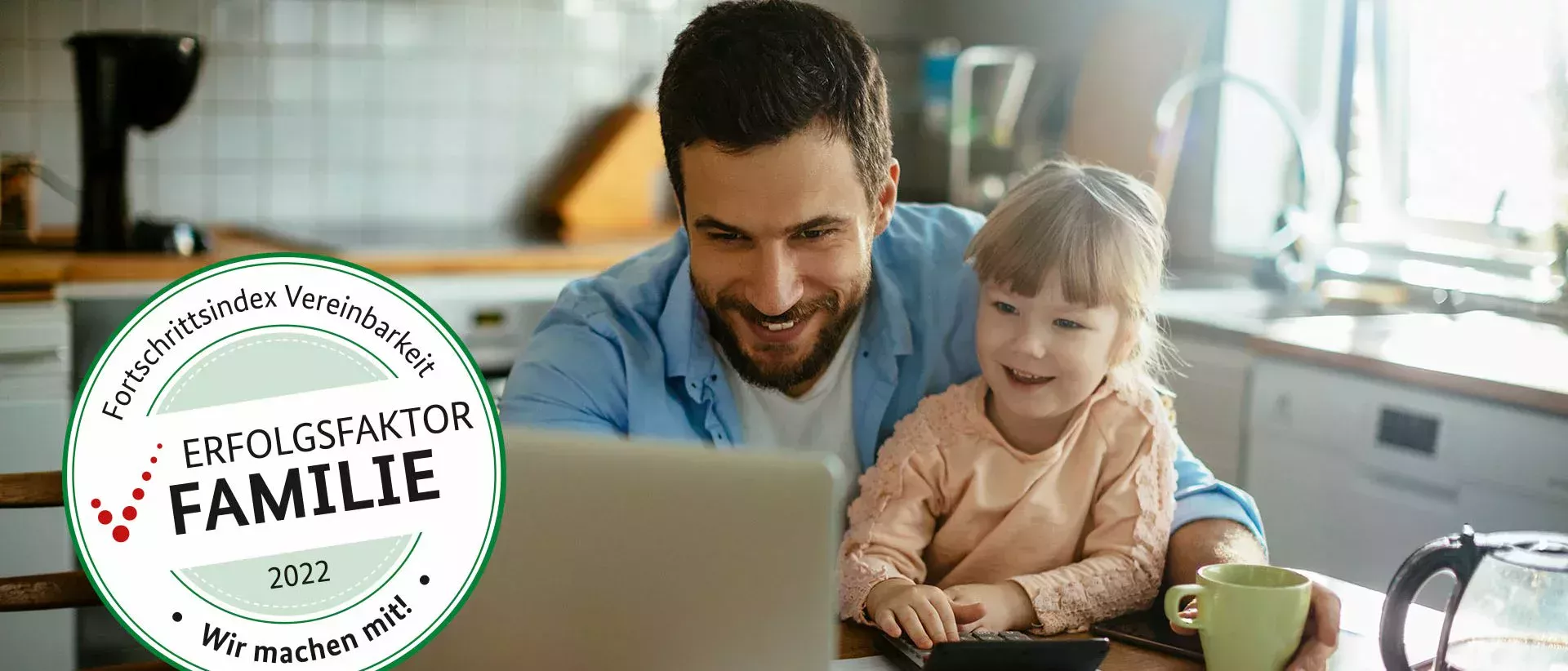 Le père est assis à la table de la cuisine avec sa petite fille et ils regardent avec bonheur l'ordinateur portable devant eux.